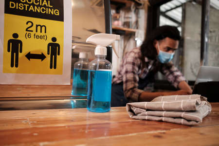 Alcohol sanitizer for healthy protection in a cafe, Asian male barista in face mask use laptop,...
