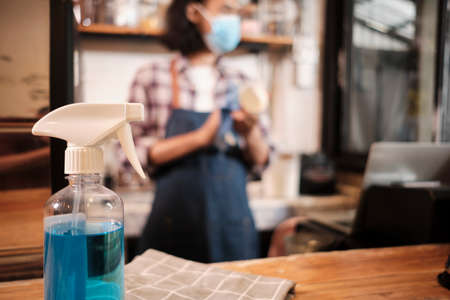 Alcohol sanitizer for healthy protection in a cafe, Asian male barista in face mask use laptop, waiting for coffee order in COVID19 pandemic quarantine, the economic impact for small business startup.の写真素材