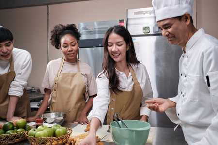 Cuisine course, senior male chef in cook uniform teaches young cooking class students to knead and roll pastry dough, prepare ingredients for bakery foods, fruit pies in stainless steel kitchen.の写真素材