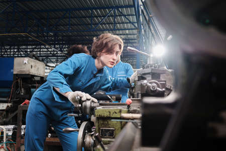 Professional young White female industry engineer worker works in safety uniform with metalwork precision tools, mechanical lathe machines, and spare parts workshop in the steel manufacturing factory.の写真素材