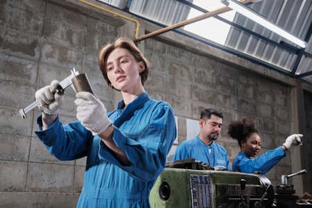 Young Caucasian female industry worker works with metalwork precision tools, lathe machines, and...