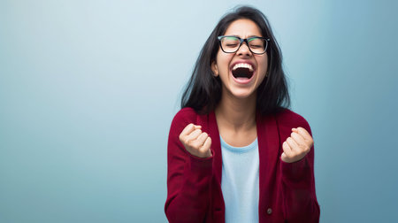 Young woman celebrating a victory on a blue background with copyspaceの素材