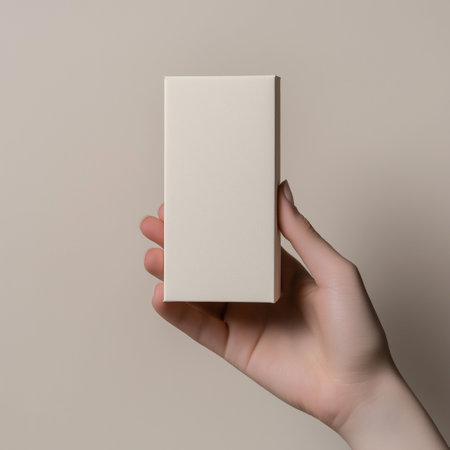 Female hand holding a blank business card on a beige background.の素材