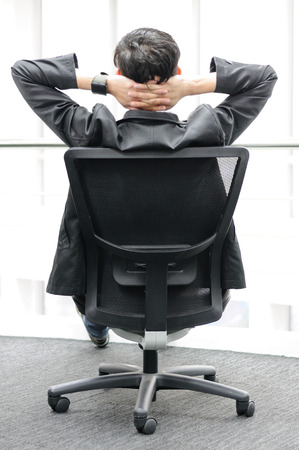 Back view of Businessman relaxing in black chairの写真素材