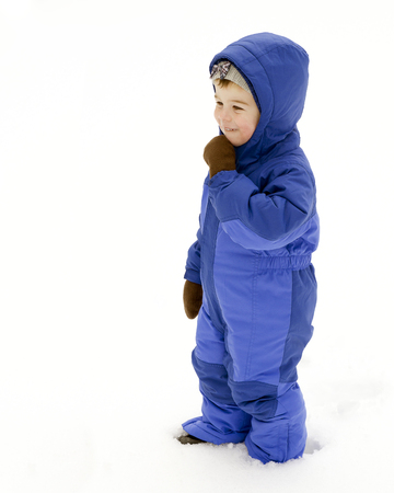 A young boy plays outside in the snow wearing a blue snowsuitの写真素材