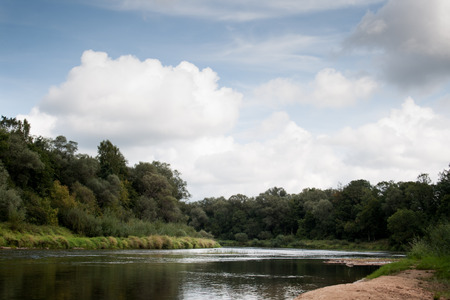 side view on wide still river in forest in summer day with blue sky and cloudsの写真素材