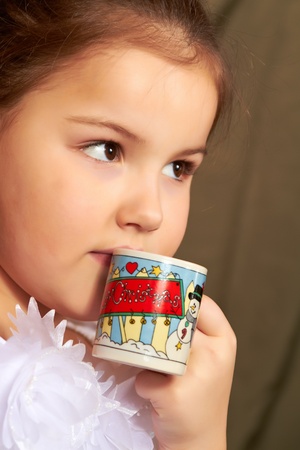 The little girl in a white dress drinks from a small cup.の写真素材
