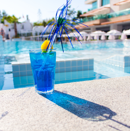Blue cocktail with its shadow and straw near the poolの写真素材