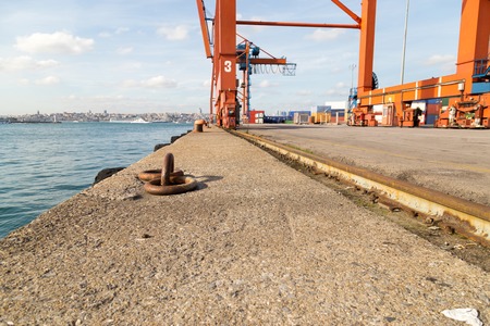 Old iron bollard over the stone dock with near the blue sea and craneの写真素材