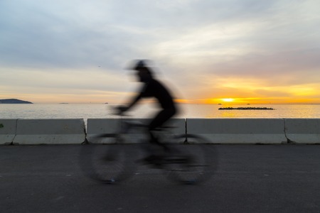 Silhouette of cyclist near the sea during the sunset with motion blurの写真素材