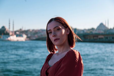 Beautiful girl with orange colored dress posing with the Galata Bridge and Mosques from Istanbulの写真素材