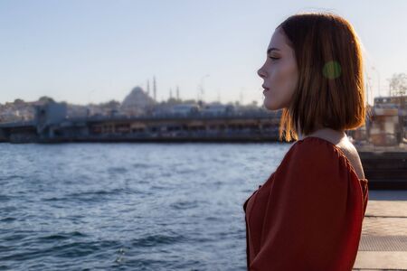 Beautiful girl with orange colored dress posing with the Galata Bridge and Mosques from Istanbulの写真素材