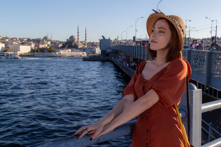 Beautiful girl with orange colored dress posing with the Galata Bridge and Mosques from Istanbulの写真素材