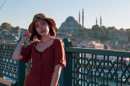Beautiful girl with orange colored dress posing with the Galata Bridge and Mosques from Istanbulの写真素材