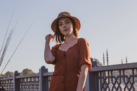 Beautiful girl with orange colored dress posing with the Galata Bridge and Mosques from Istanbul