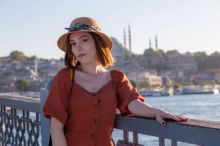 Beautiful girl with orange colored dress posing with the Galata Bridge and Mosques from Istanbul