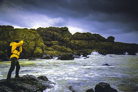 Outdoor photographer taking a photo over rocks among waves gloomy sky with dramatic cloudsの写真素材