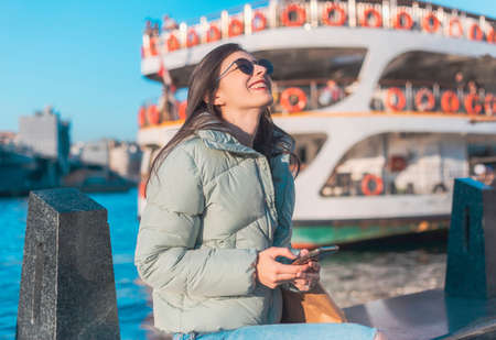 Cheerful brunette woman looking to her mobile phone and smiling in a street copy space
