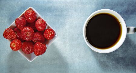 Flatlay top view a bowl of fresh strawberry, a cup of coffee on modern concrete background with trend colorの写真素材