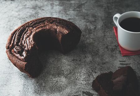Dark and moody illuminated cake baked with cake mold circle and a cup of coffee with rustic backdropの写真素材