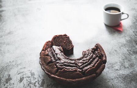 Dark and moody illuminated cake baked with cake mold circle and a cup of coffee with rustic backdropの写真素材