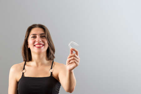 Beautiful smiling Turkish woman is holding an invisalign bracer, Isolated studio shot with copy spaceの写真素材