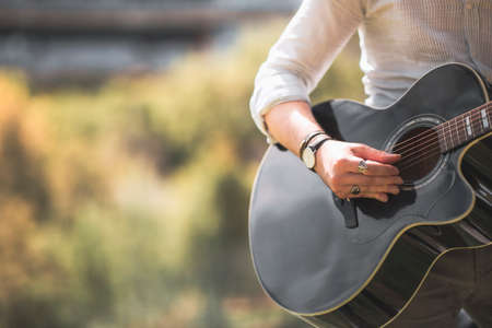 Anonymous man is playing a guitar at outside in autumn season with trendy orange colors, headless photo with copy space.の写真素材