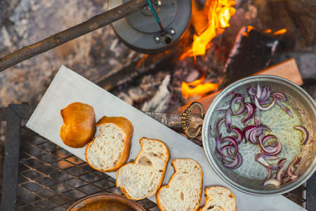 Flat lay view of camp fire cooking, breads are in a row, a tea pot and onion pan is on the fire