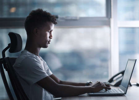 Young handsome black man concentrated focused to his laptop and working in serious mood in a modern office. copy space include profile shot.の写真素材