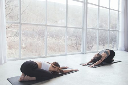 Two beautiful women performing synchronised yoga in a modern studio