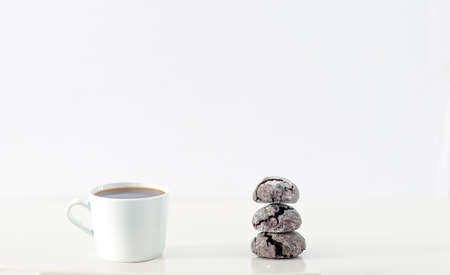 Minimal designed scene, a coffee cup and dark chocolate cookie over plain white background, includes...