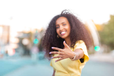 Happy and cheerful Afro Black Woman with her curly hair is posing in a street among the car and...