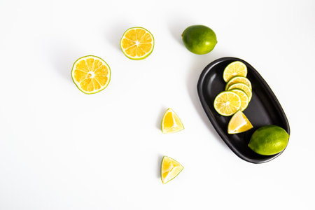 Flat lay view green lime lemons over dark backdrop with black plate.Includes copy space.の写真素材