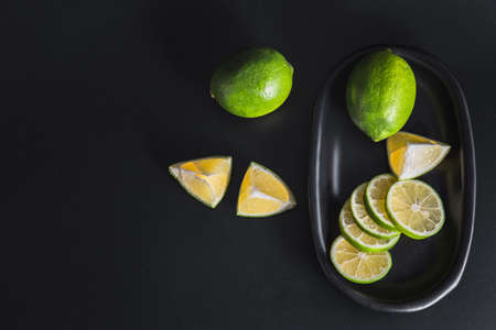 Flat lay view green lime lemons over dark backdrop with black plate.Includes copy space.の写真素材
