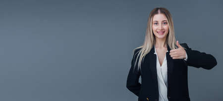 Beautiful blonde business woman portrait, she gestures thumbs up. She has warm smiles, includes copy space.の写真素材