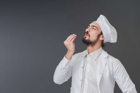 Amazed young male Italian handsome chef. He is Gesturing delicious sign, studio shot includes copy space.の写真素材