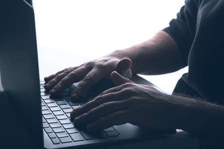 Cyber crime concept with copy space: Anonymous man is using a laptop with reverse lighting.