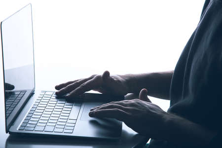 Cyber crime concept with copy space: Anonymous man is using a laptop with reverse lighting.