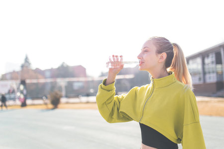 Young woman drinking water after jogging in the city. Healthy lifestyle concept.