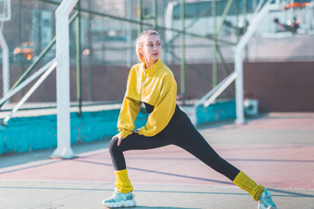 young beautiful sportive woman doing stretching exercise on sports ground in cityの写真素材