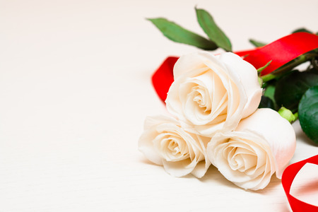 White roses with red ribbon on a light wooden background. Women' s day, Valentines Day, Mothers day. Copy space, selective focusの写真素材