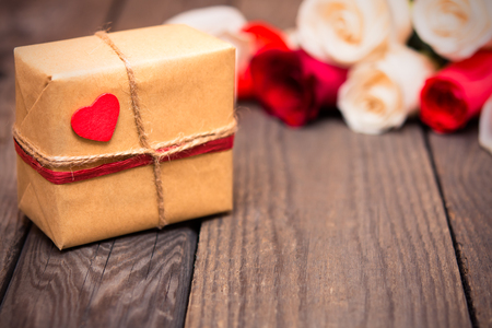 Gift box with blured red and white roses on a dark wooden background. Women' s day, Valentines Day, Mothers day. Copy space, selective focus. Natural optical blur, tonedの写真素材