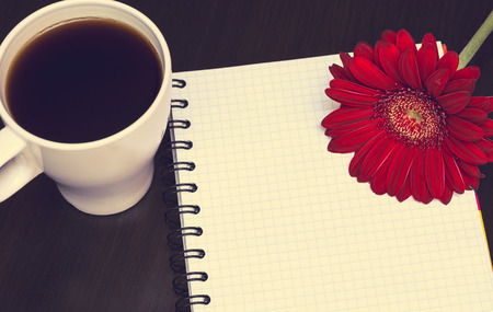 Red gerbera flower,cup of coffee and notebook on the wooden desk. Selective focus, tonedの写真素材