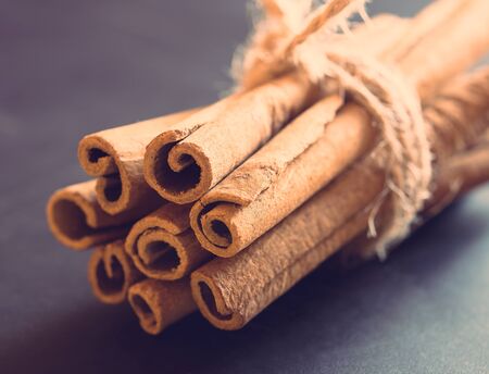 Bunch of cinnamon sticks on black background. Selective focus, toned