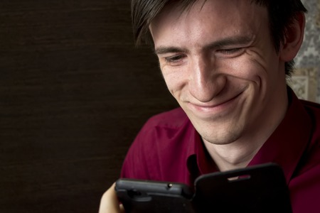 Happy young man in a purple shirt looking at a black smartphone smiling broadlyの写真素材