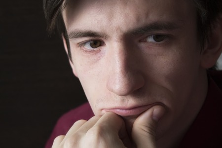 A close-up portrait of a guy, a fist propping his cheekの写真素材