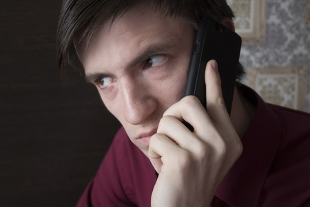 A young man with black smartphone, with an alarming suspicious lookの写真素材