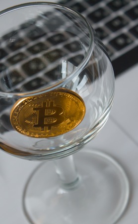 golden bitcoin in a cocktail glass on laptop backgroundの写真素材