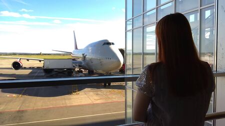 the girl looks out the window at the plane, awaits boarding the plane, meeting at the airportの写真素材