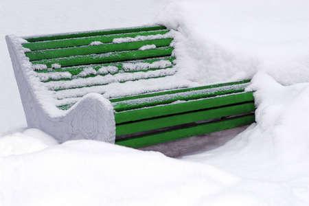 Big green wooden bench buried in snow and partly cleaned.の写真素材
